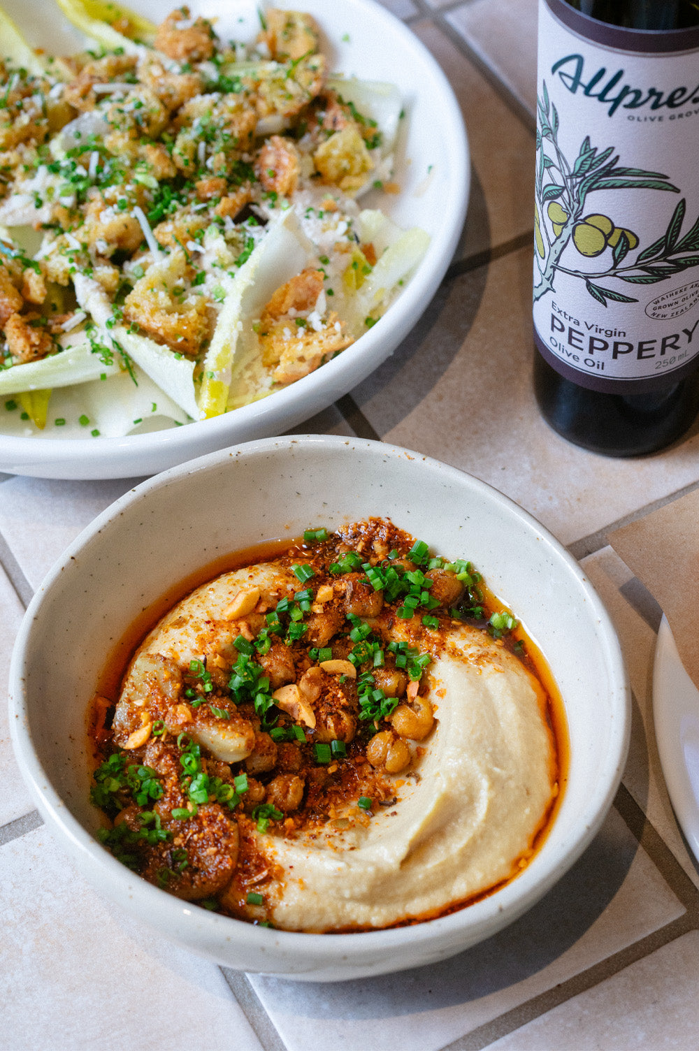 Bowl of hummus next to a bottle of Allpress olive oil