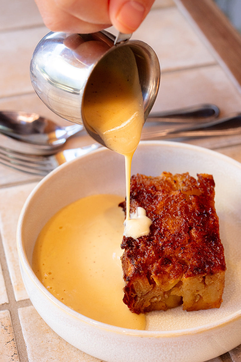 Creme Anglaise poured onto a bread and butter pudding at Bistro Allpress