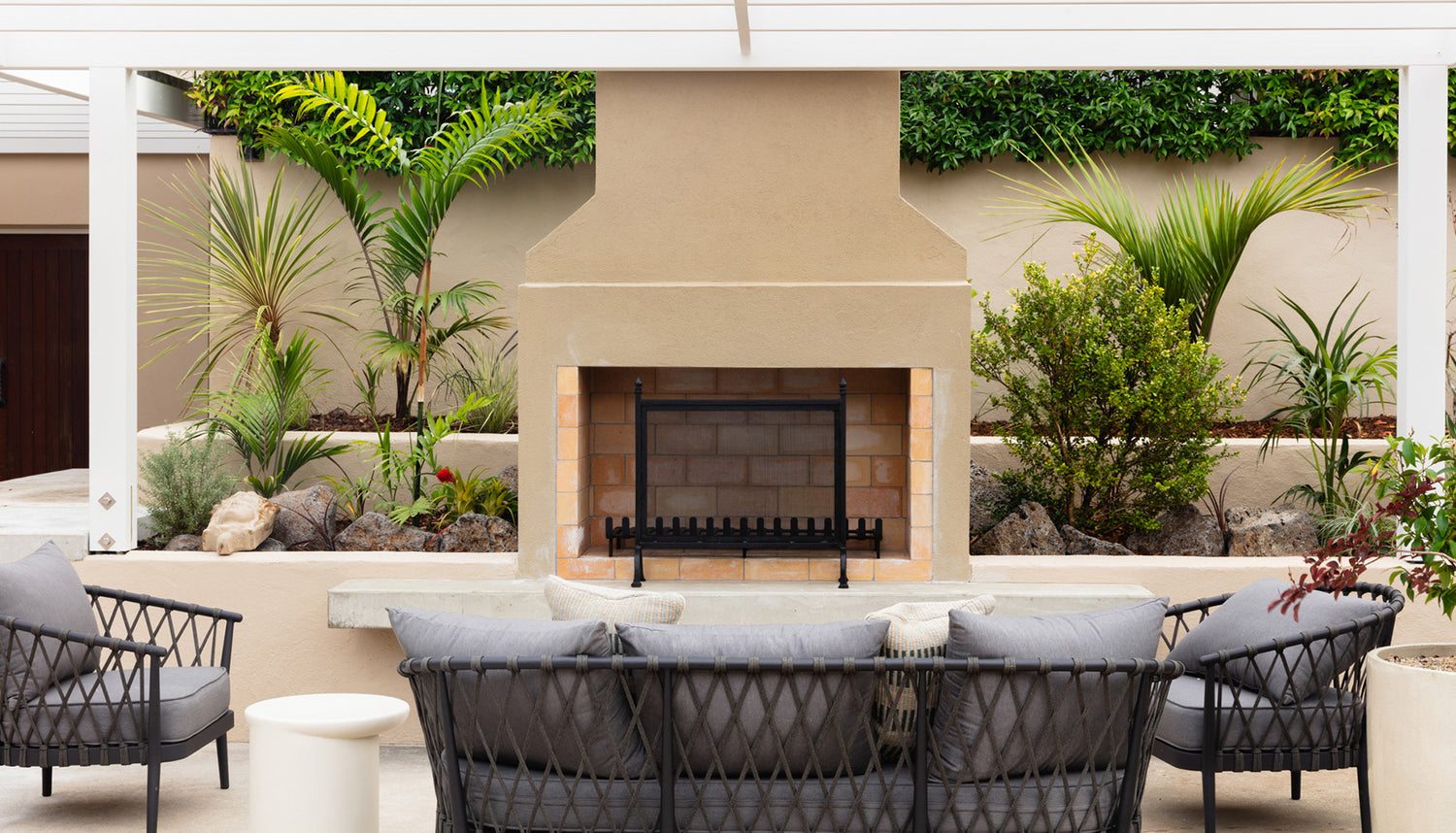 Outdoor patio area with chairs, table, and fireplace surrounded by plants on Waiheke Island