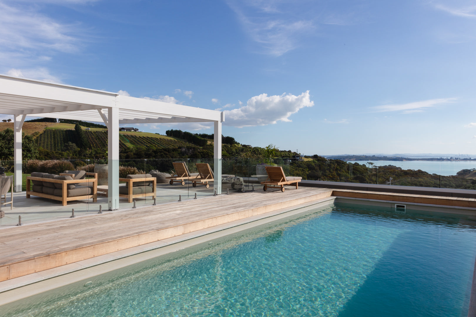 Outdoor pool and wooden deck with chairs overlooking the Hauraki Gulf on Waiheke Island