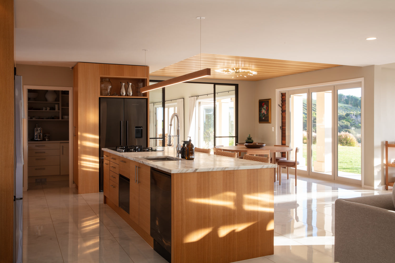 Modern kitchen with wooden cabinetry and marble island, large windows overlooking the Hauraki Gulf