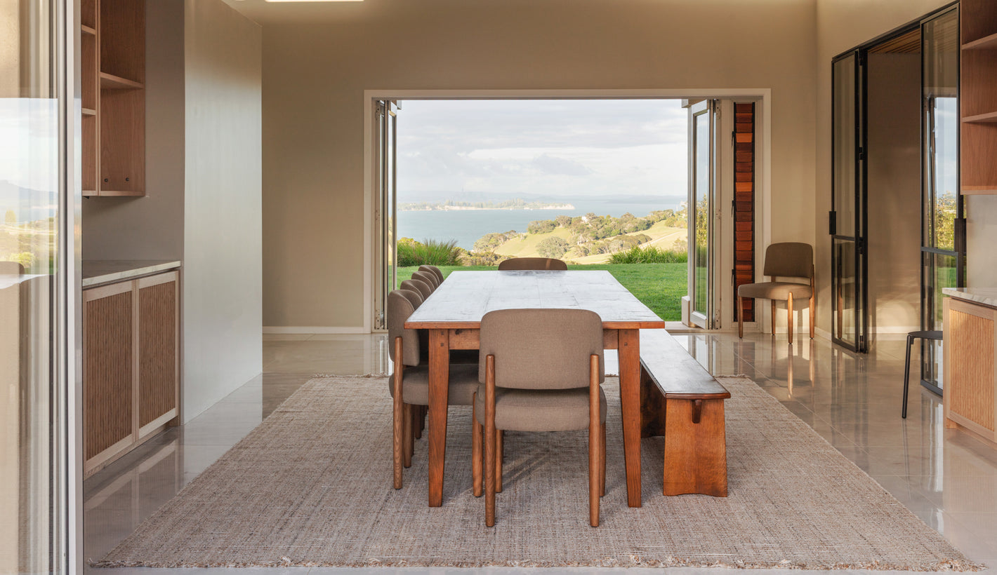 Modern dining area with wooden table and chairs in a home with large glass doors leading to a view of the Hauraki Gulf